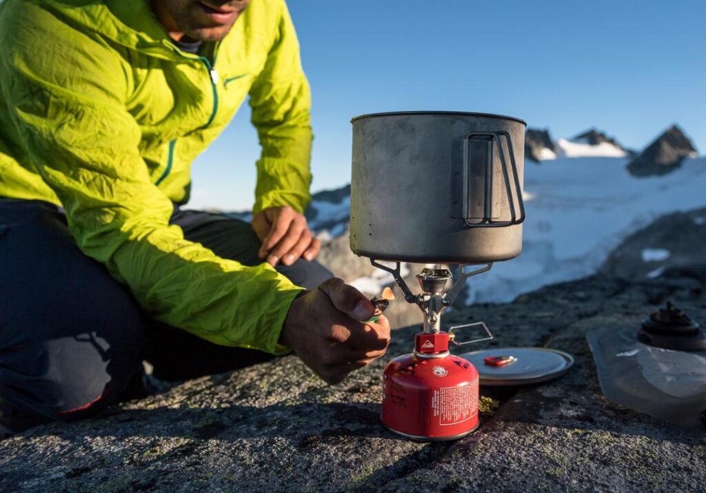 A person in a green jacket cooking on a gas Pocket Rocket MSR stove.